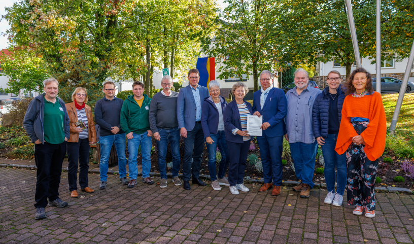 Der Kreisbeigeordnete übergibt den Förderbescheid an die Bürgermeisterin, drumherum weitere Beteiligte